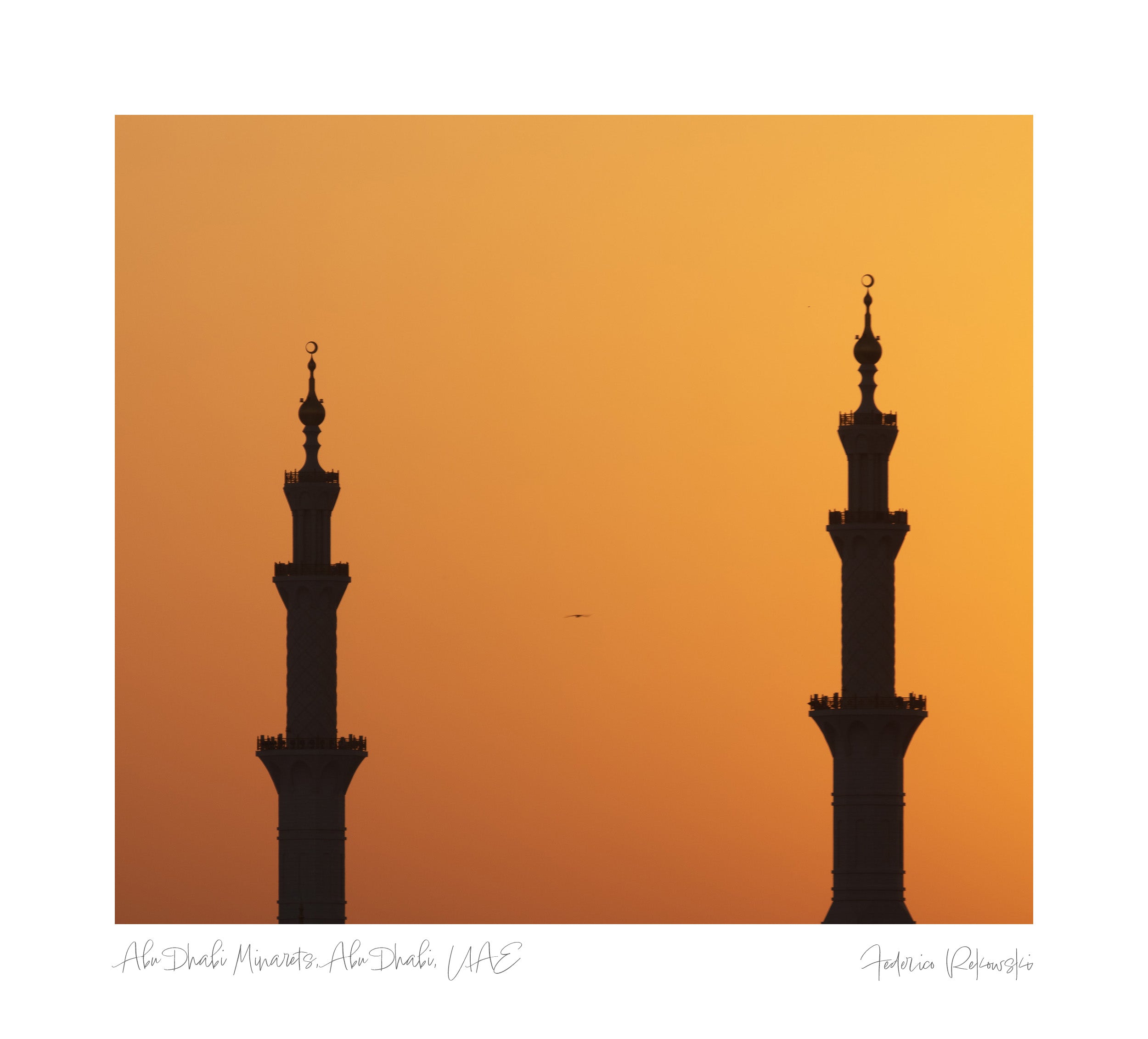 Silhouettes of two minarets against an orange sunset sky in Abu Dhabi.