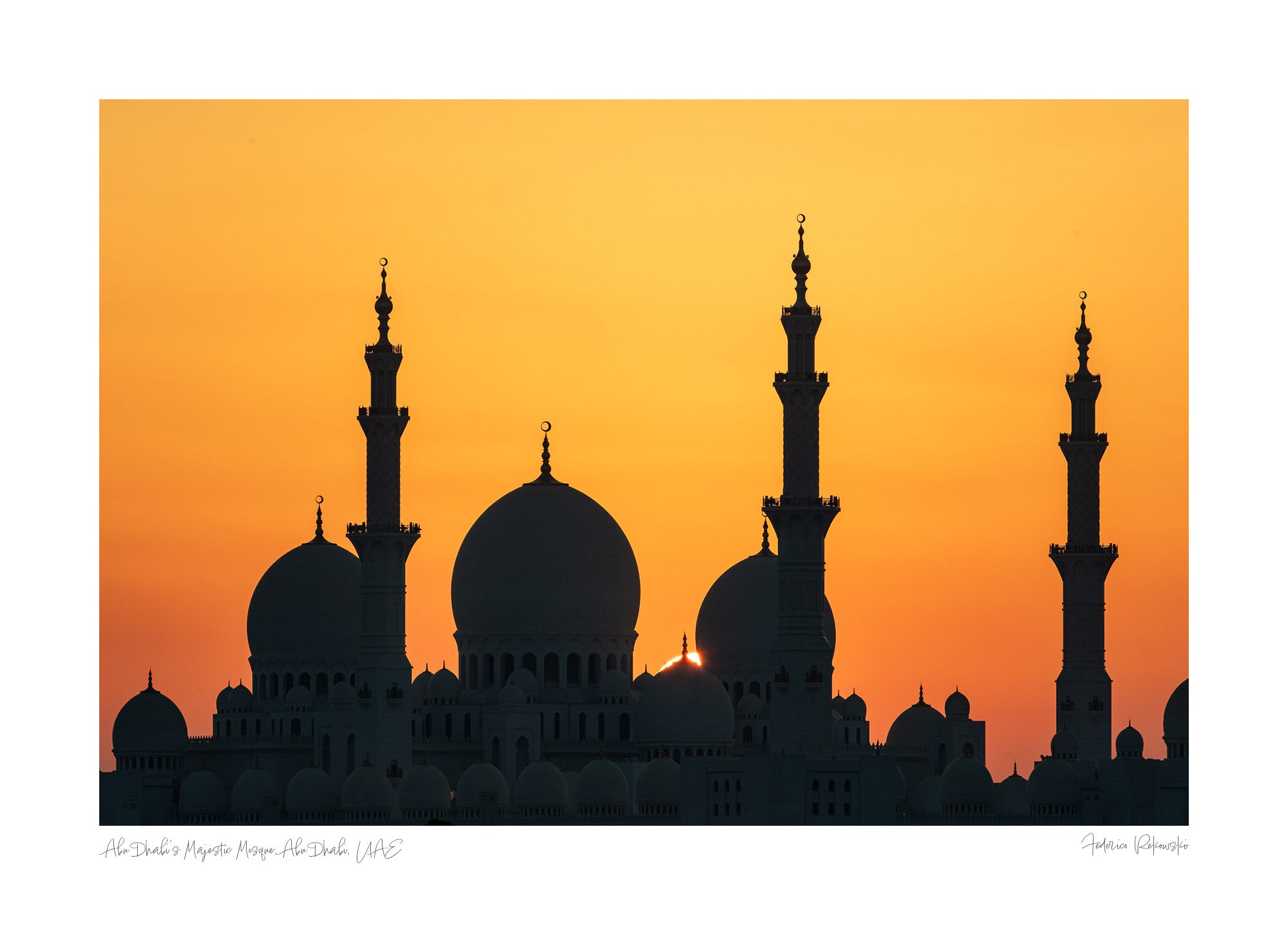 Silhouette of a grand mosque with multiple domes and minarets against a bright orange sunset sky in Abu Dhabi.