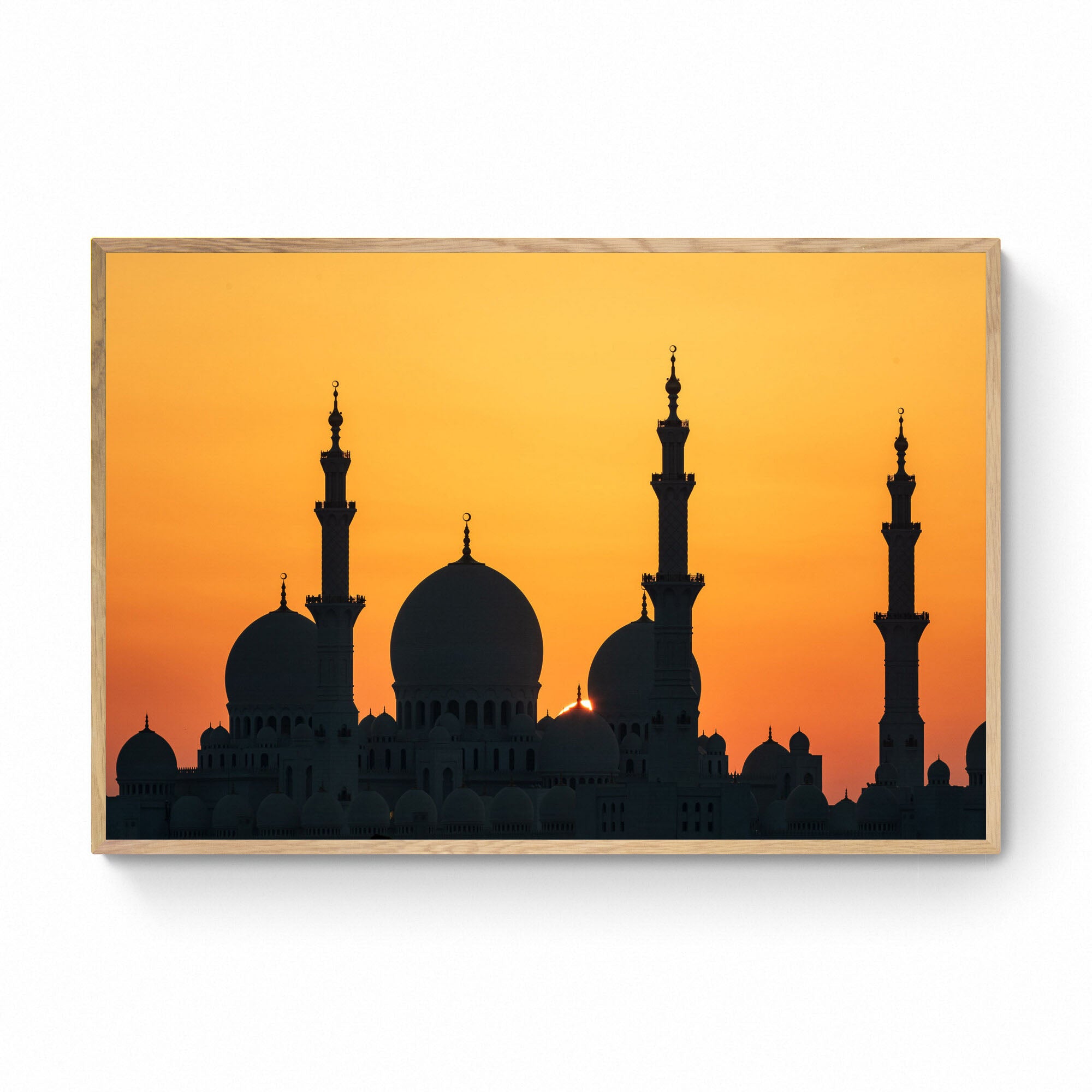 Silhouette of a grand mosque with multiple domes and minarets against a bright orange sunset sky in Abu Dhabi.