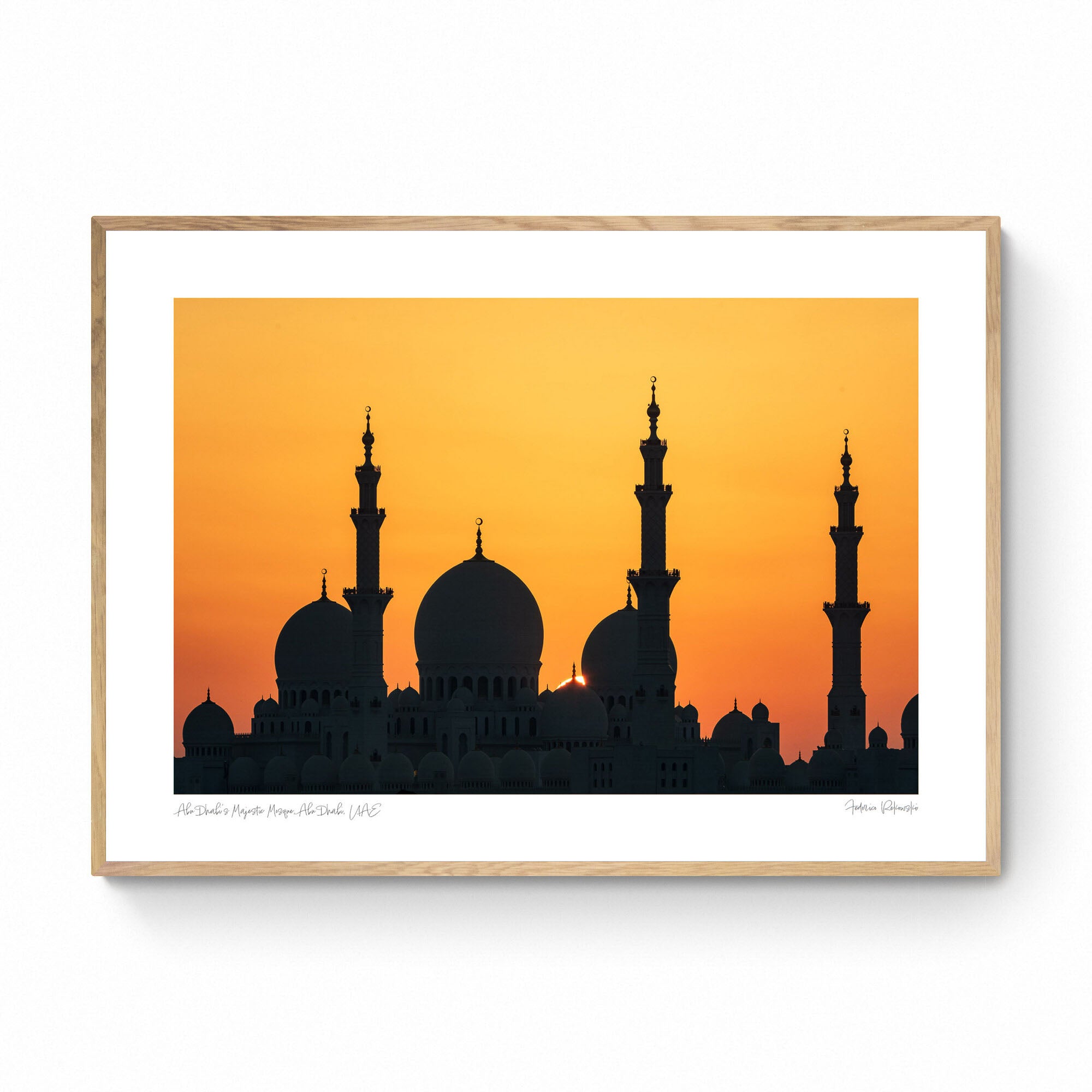 Silhouette of a grand mosque with multiple domes and minarets against a bright orange sunset sky in Abu Dhabi.