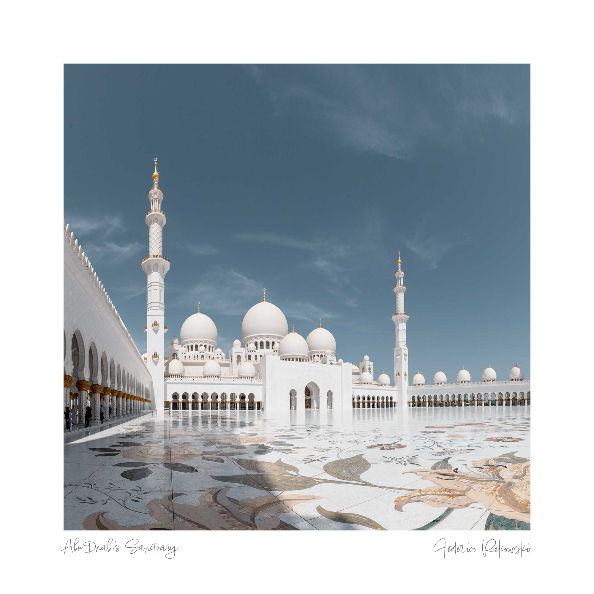 The Sheikh Zayed Grand Mosque in Abu Dhabi with its white marble domes and minarets, reflected on the glossy courtyard surface under a clear blue sky.