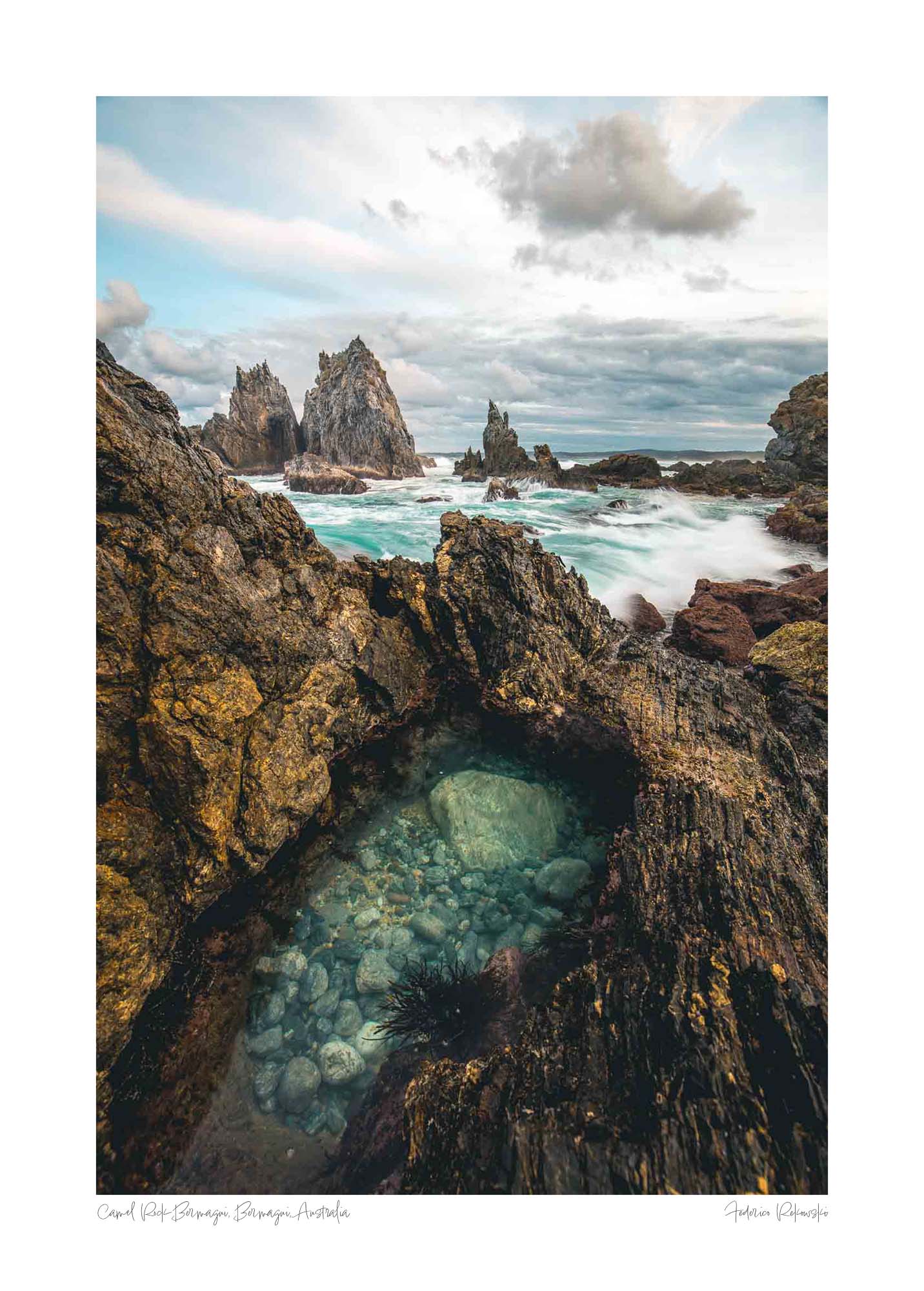 Rugged rock formations of Camel Rock in Bermagui with a natural tide pool in the foreground and turbulent sea in the background under a cloudy sky.