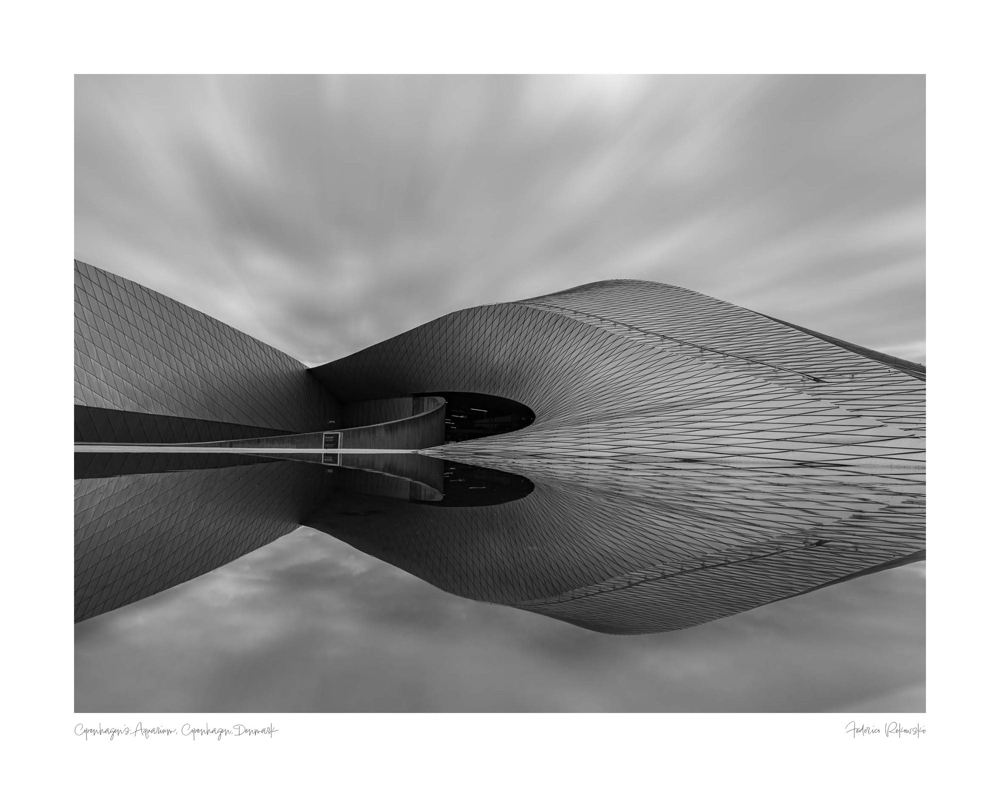 Black and white image of The Blue Planet Aquarium in Copenhagen with its reflective, wavy facade against a blurred sky.