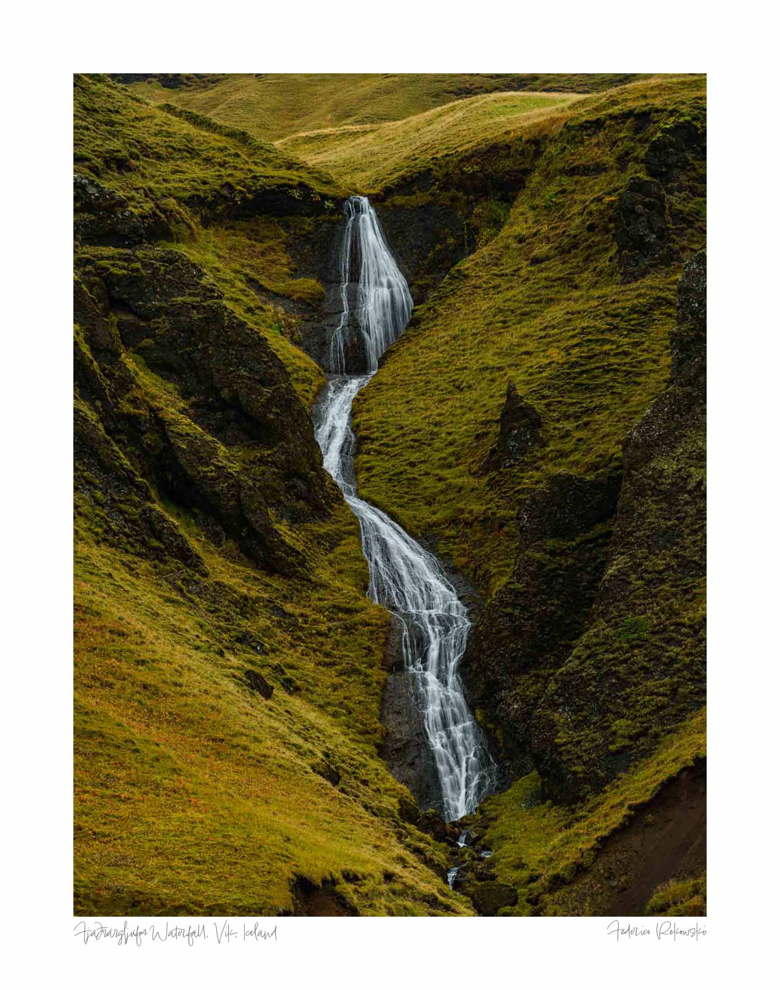 A hidden waterfall flows through the green, mossy cliffs of Fjaðrárgljúfur canyon in Iceland.