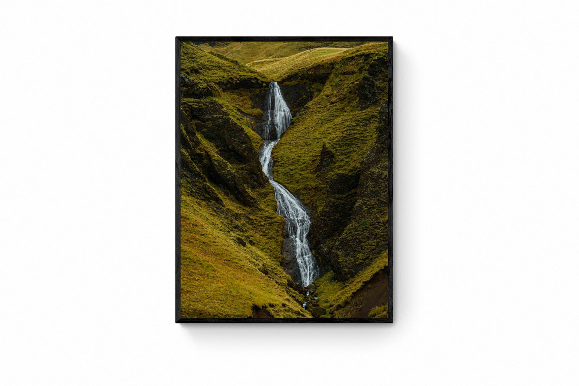 A hidden waterfall flows through the green, mossy cliffs of Fjaðrárgljúfur canyon in Iceland.