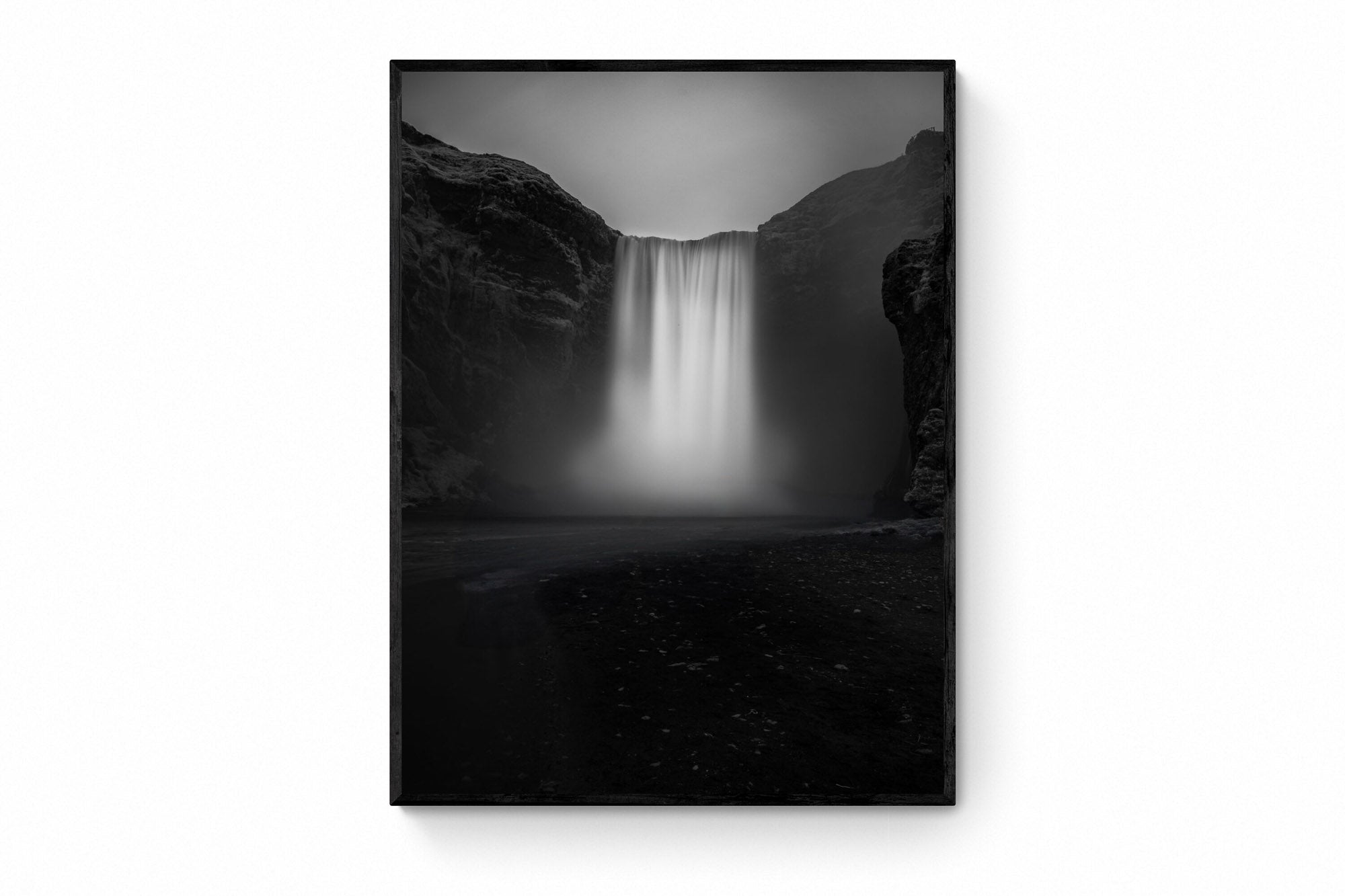 A long exposure photograph of Skógafoss waterfall in Iceland, rendered in stunning black and white, capturing the smooth flow of water between two dark cliffs.