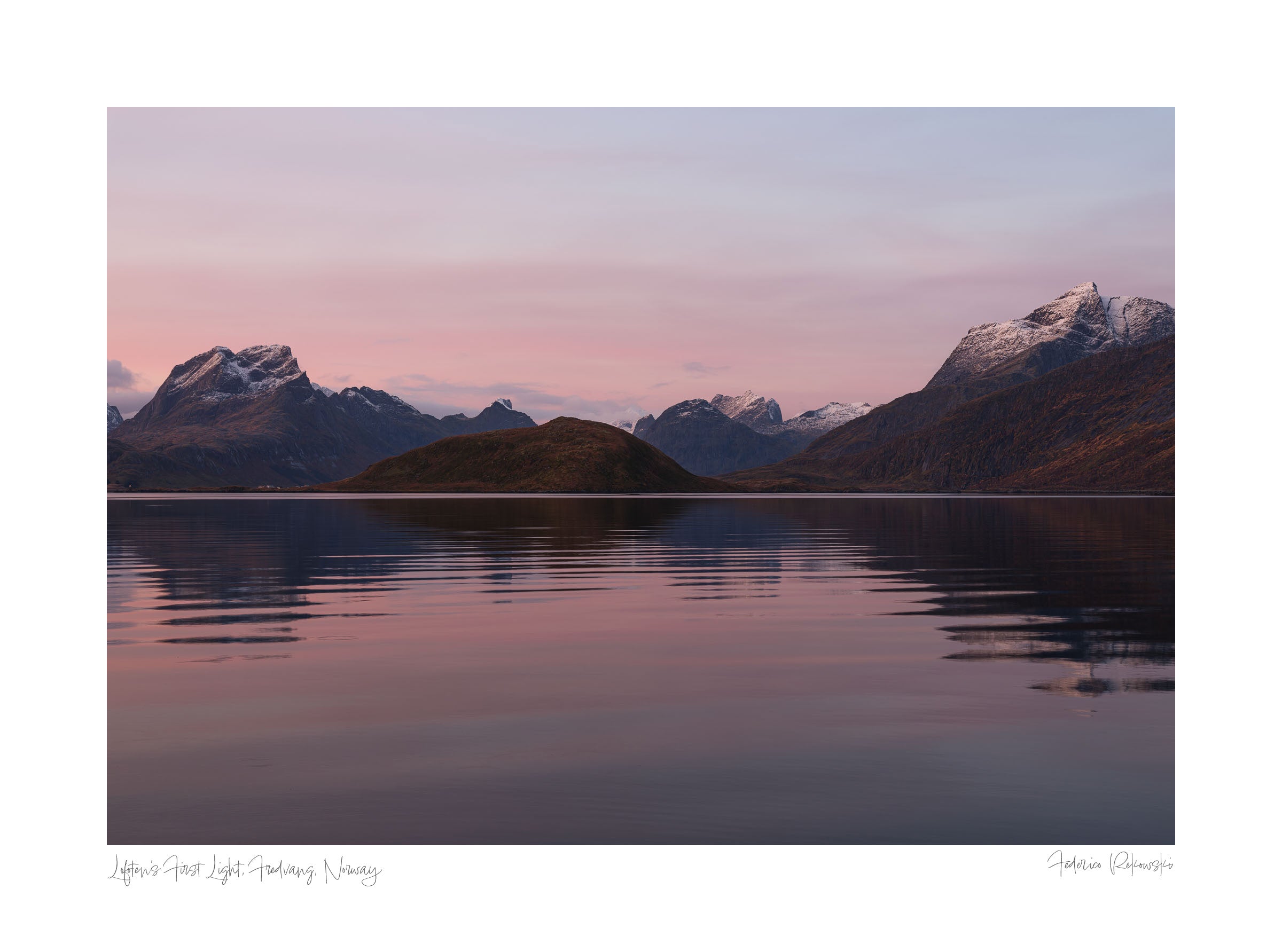 Sunrise at Fredvang in Lofoten, with snow-capped mountains reflecting in calm waters under a pastel-hued sky.