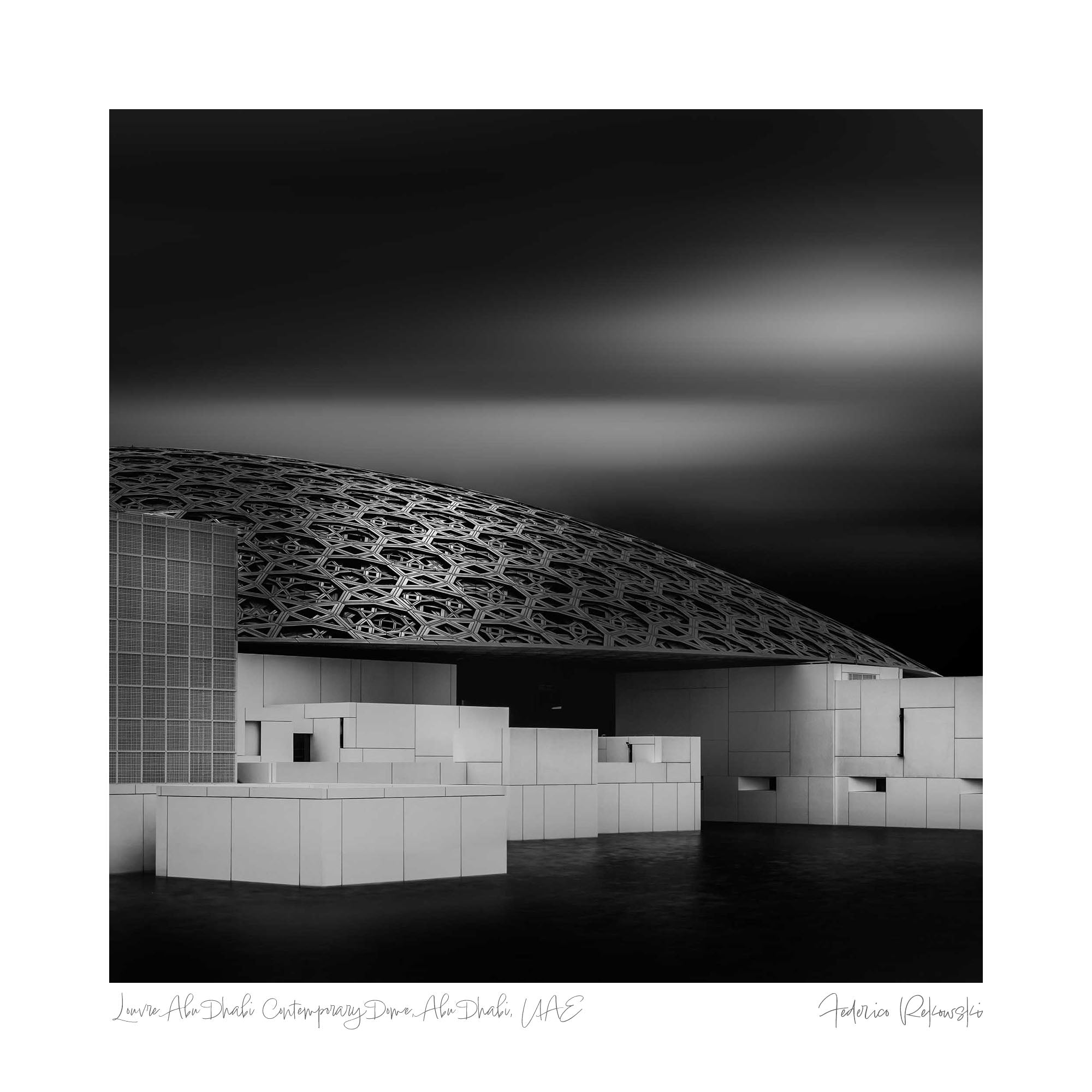 Black and white photo of the Louvre Abu Dhabi, highlighting the intricate geometric patterns of the dome against a dramatic sky.