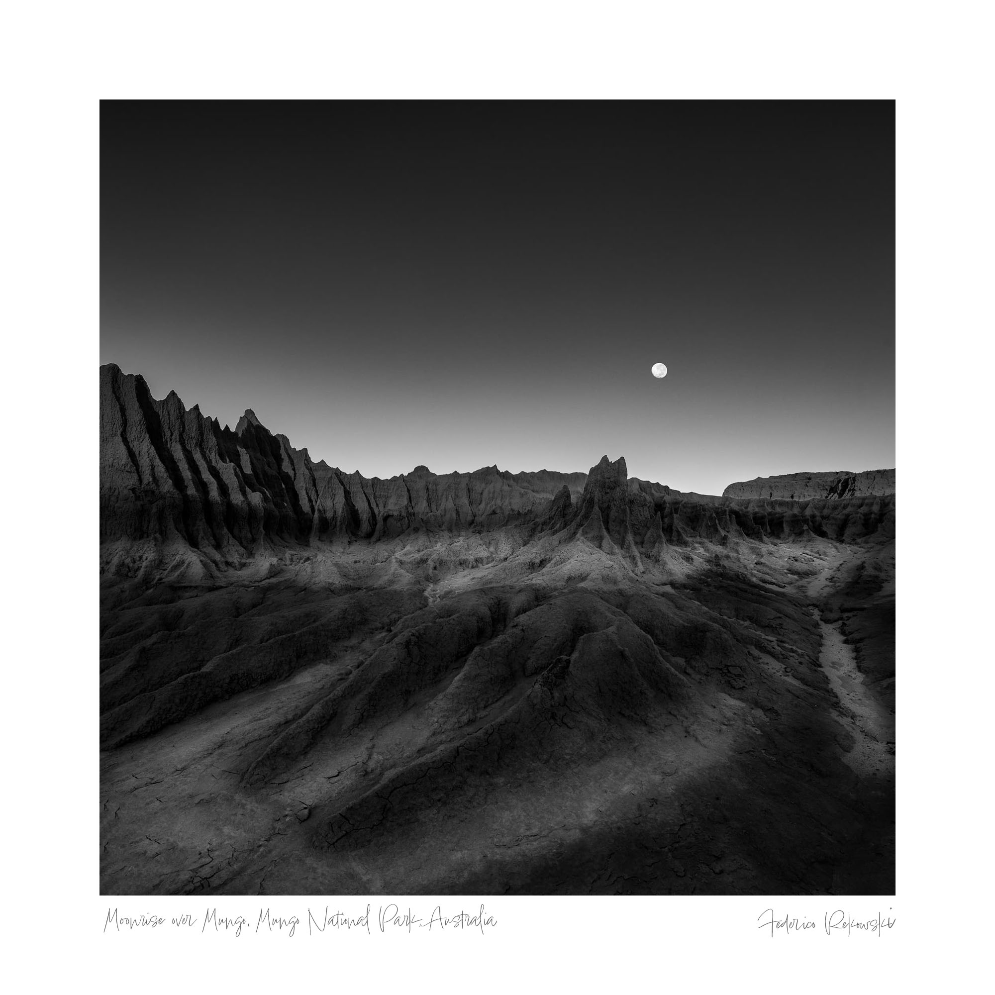 Black and white photo titled "Moonrise Over Mungo," depicting the moon rising above the dramatic landscapes of Mungo National Park, Australia.