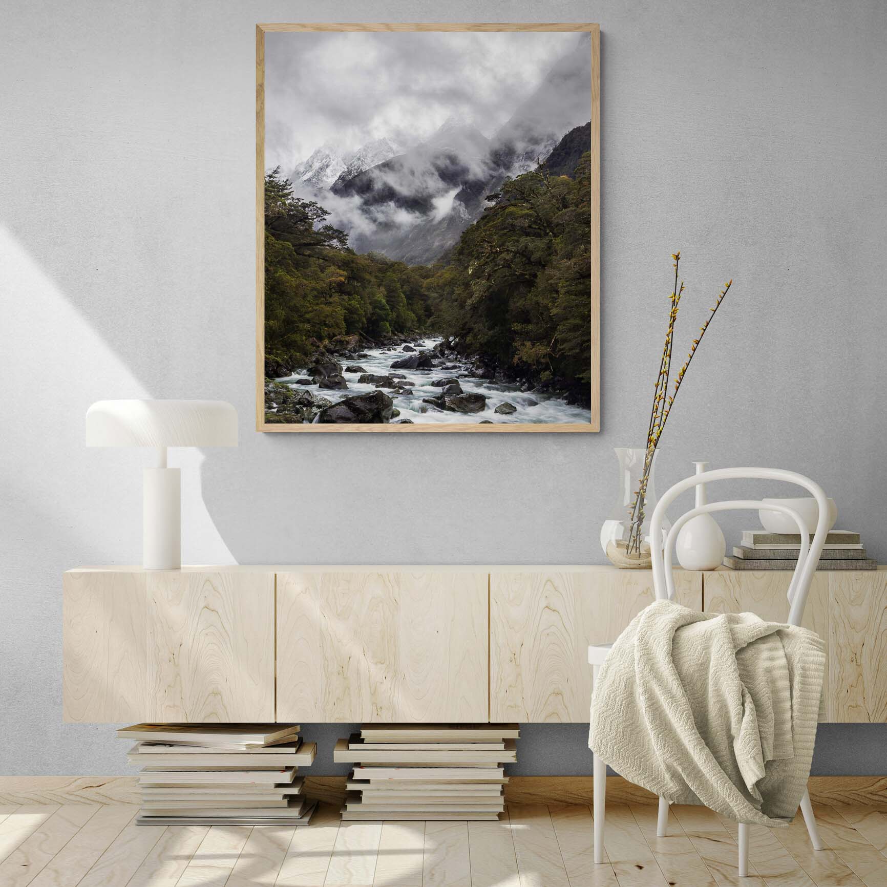 A powerful river cuts through a verdant forest with snow-covered mountains enshrouded in mist in the background at Milford Sound, New Zealand. Frame on a living Room