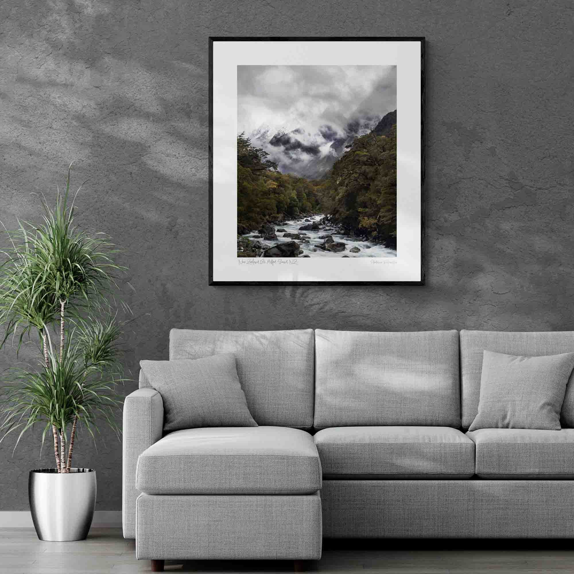 A powerful river cuts through a verdant forest with snow-covered mountains enshrouded in mist in the background at Milford Sound, New Zealand. Frame on a living Room