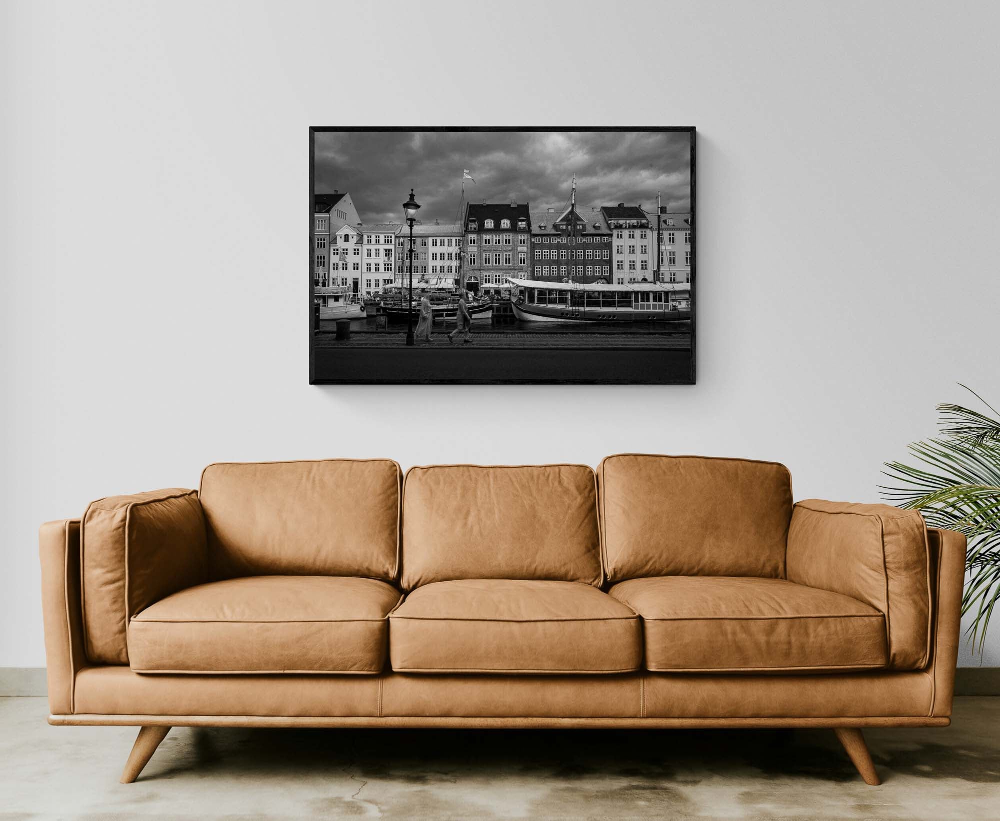 Black and white image of Nyhavn, Copenhagen, with historical buildings along the waterfront, boats docked in the canal, and people walking by.