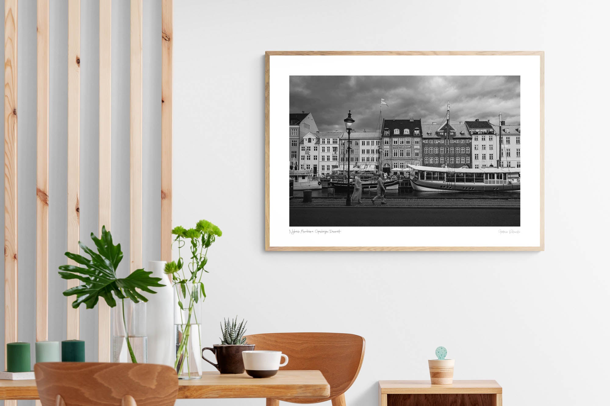 Black and white image of Nyhavn, Copenhagen, with historical buildings along the waterfront, boats docked in the canal, and people walking by.