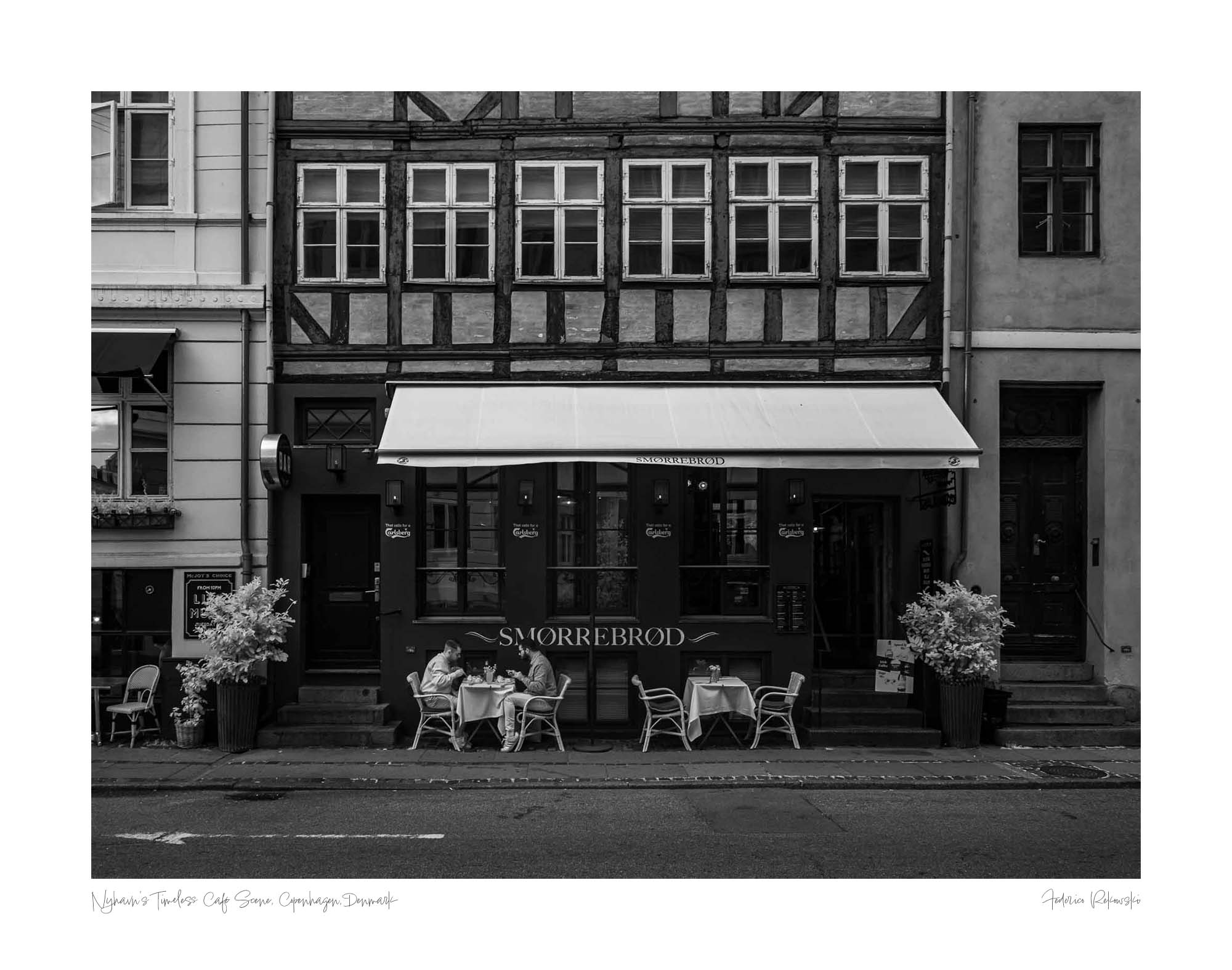 Black and white photo of a traditional Danish Smørrebrød café in Nyhavn, Copenhagen, with outdoor seating and historical buildings.