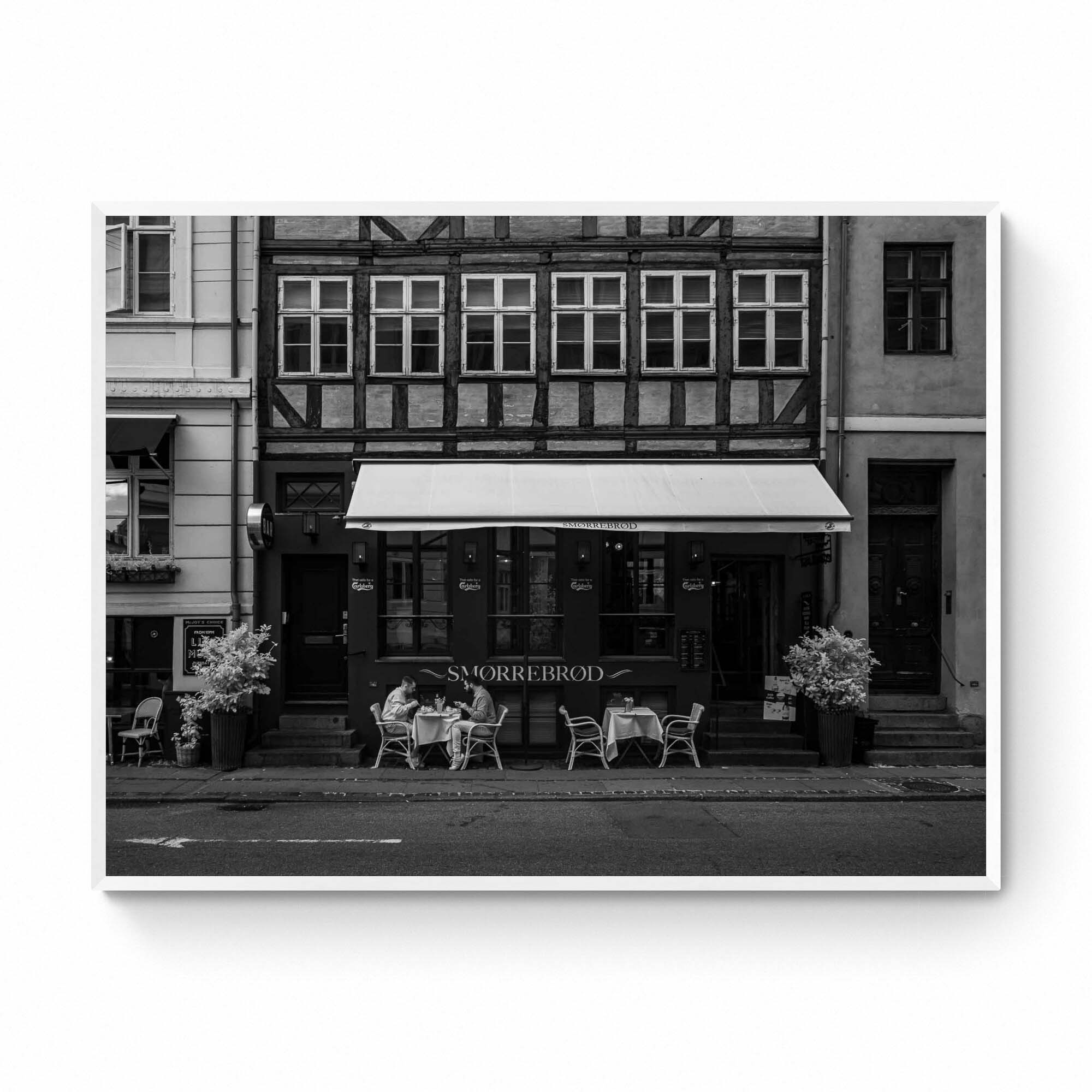 Black and white photo of a traditional Danish Smørrebrød café in Nyhavn, Copenhagen, with outdoor seating and historical buildings.