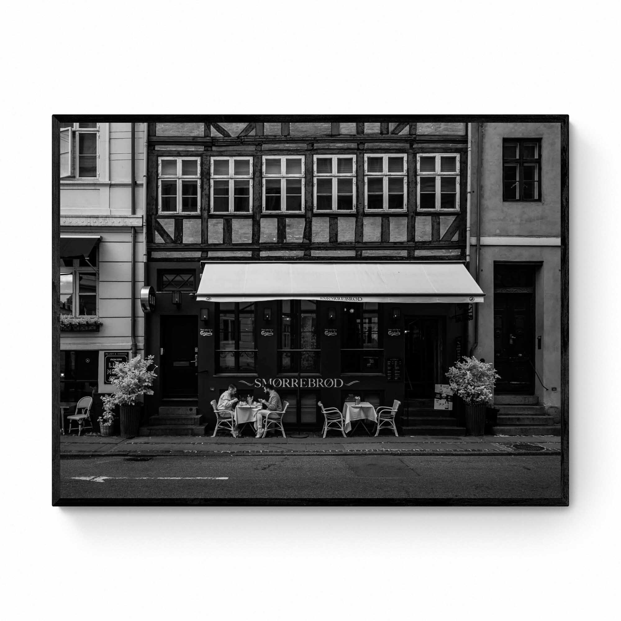 Black and white photo of a traditional Danish Smørrebrød café in Nyhavn, Copenhagen, with outdoor seating and historical buildings.