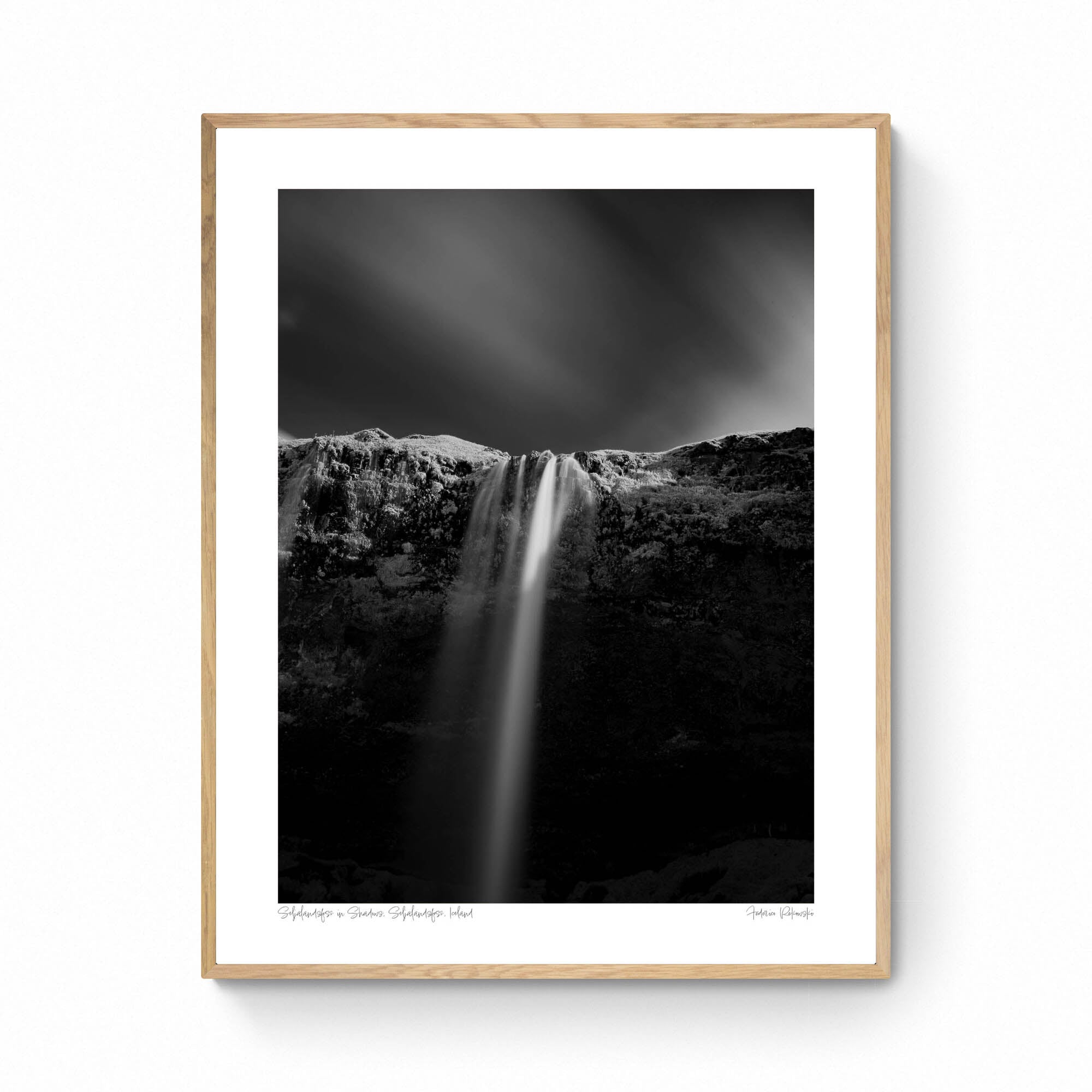 A black and white long-exposure photograph of Seljalandsfoss waterfall in Iceland, showing smooth water streams against a dark, textured cliff.