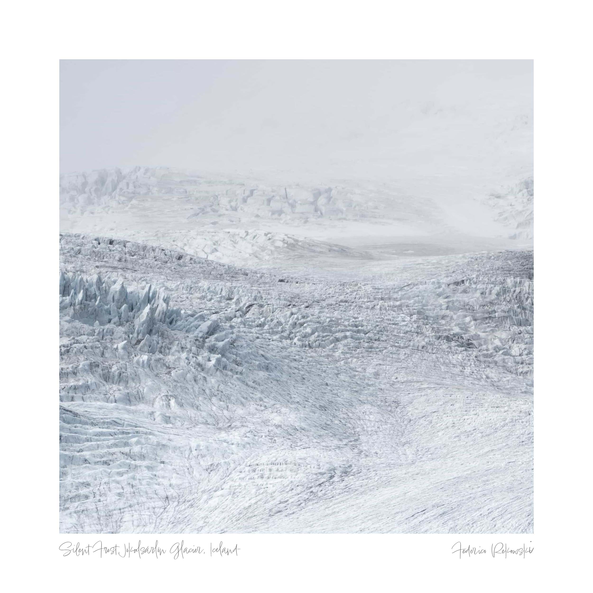 A monochromatic view of an expansive glacier in Iceland, showing textured ice formations under a subtle gray sky.