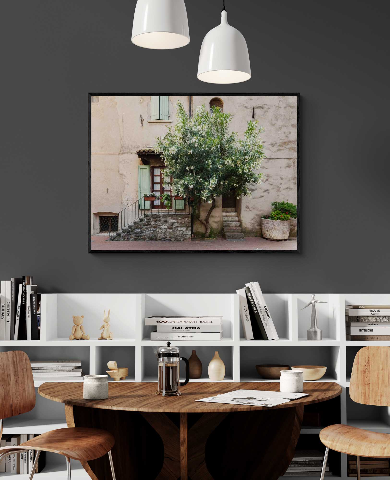 Quaint Italian house with a flowering oleander tree, stone steps, green shutters, and a large potted plant in Sirmione, Italy.