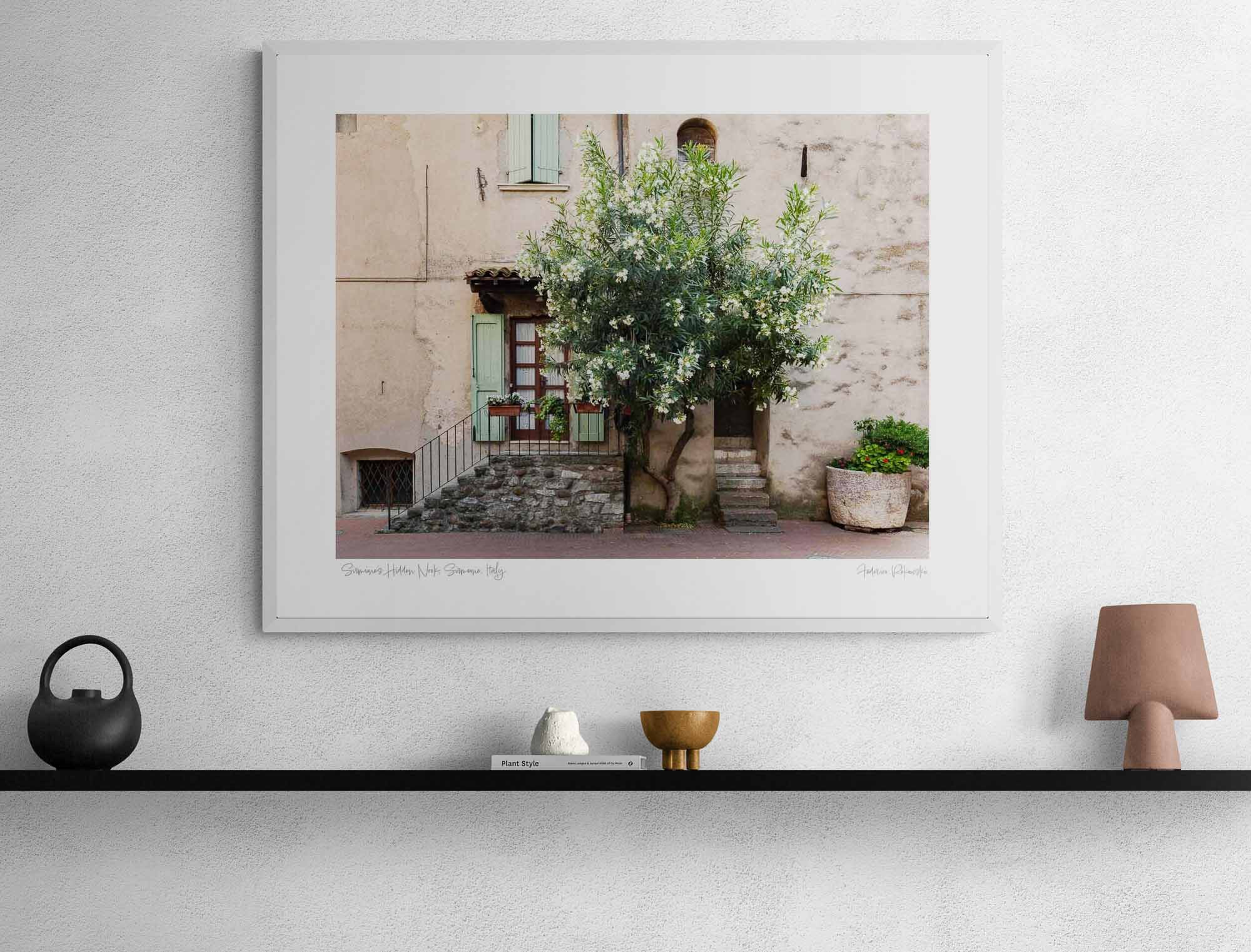 Quaint Italian house with a flowering oleander tree, stone steps, green shutters, and a large potted plant in Sirmione, Italy.