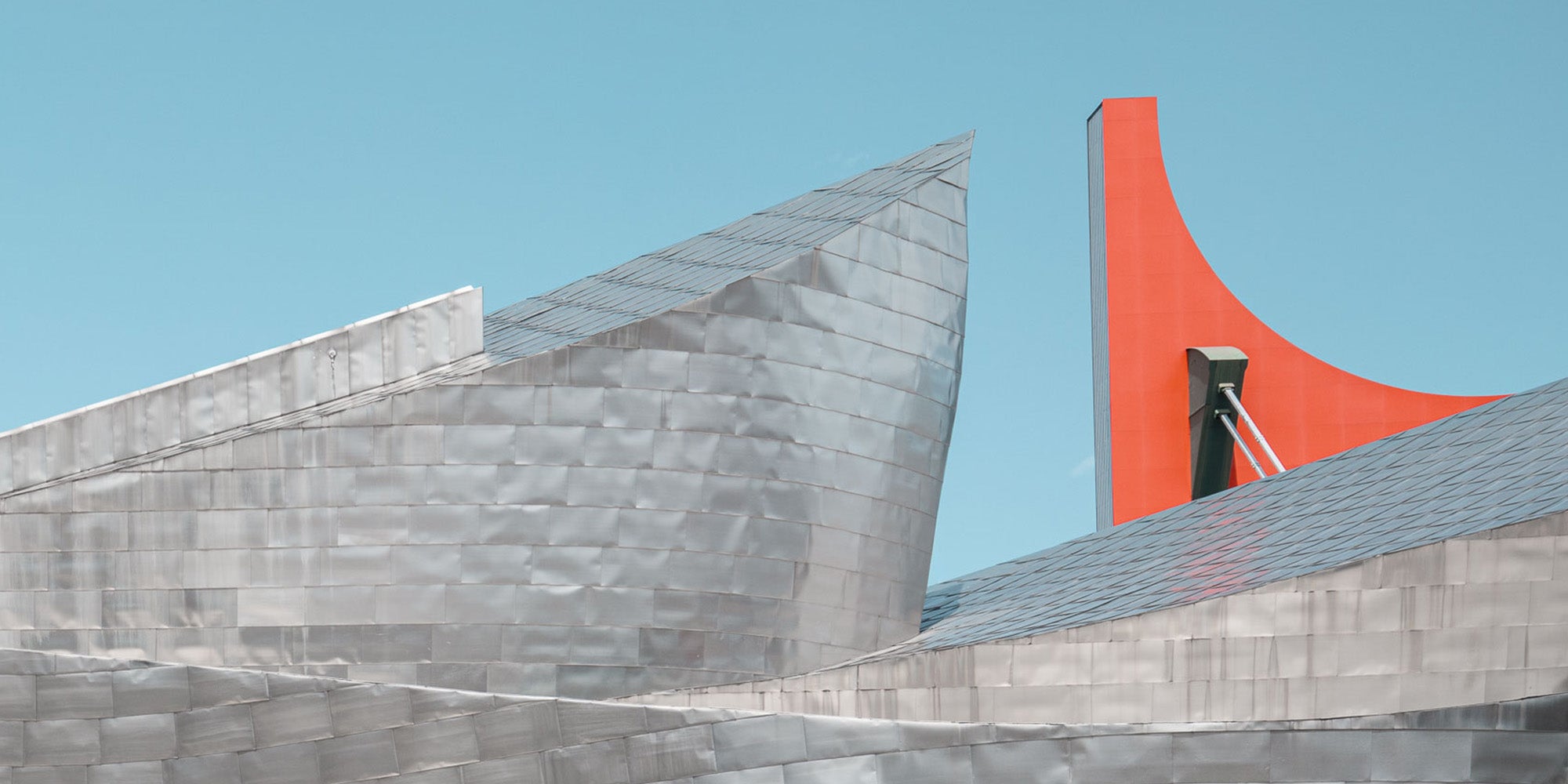 The Guggenheim Museum Bilbao, with its metallic curves contrasted by a bright red architectural feature against a clear blue sky.