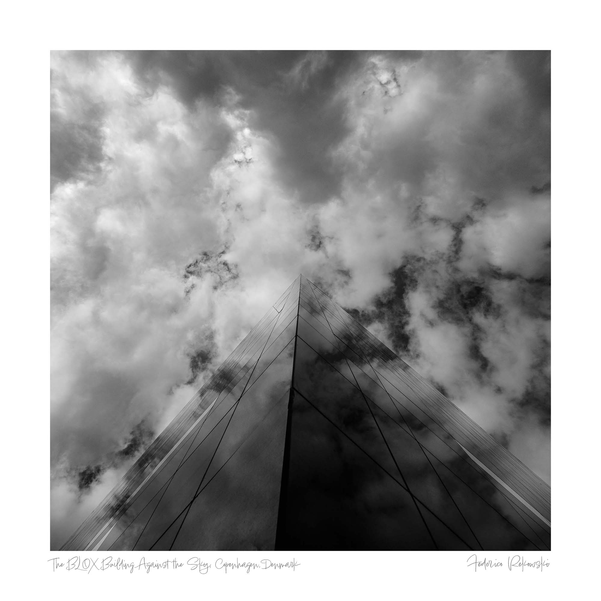 "Black and white photo of the BLOX building in Copenhagen, with its reflective glass facade reaching into a dramatic sky."