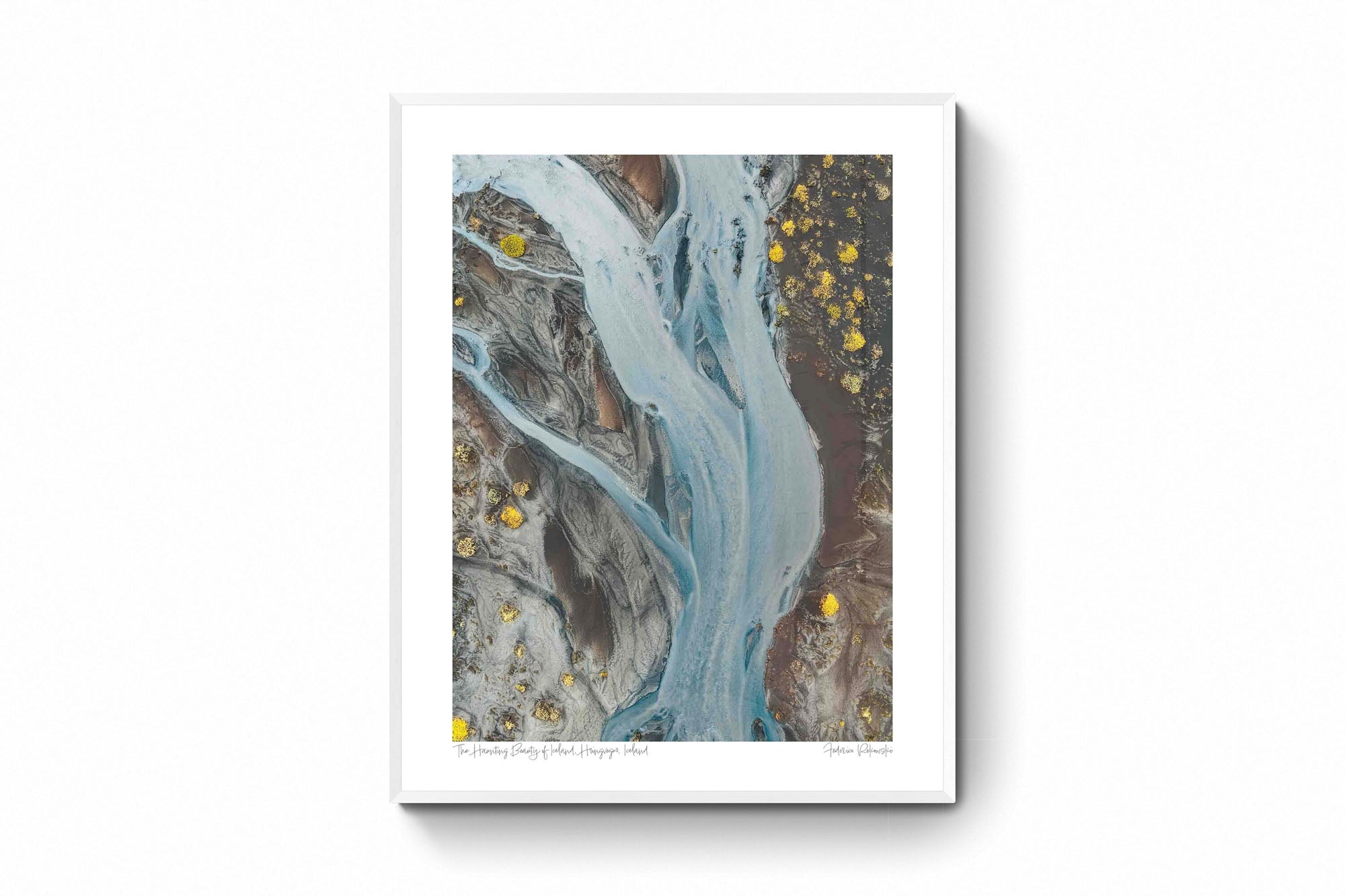 Aerial photo of a ghostly pale blue river snaking through the darker earth in Iceland, with patches of bright yellow flora.