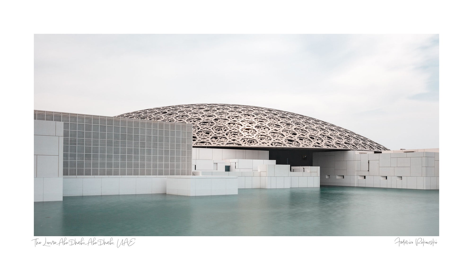 Wide-angle view of the Louvre Abu Dhabi’s intricate dome over calm water, under a soft sky.