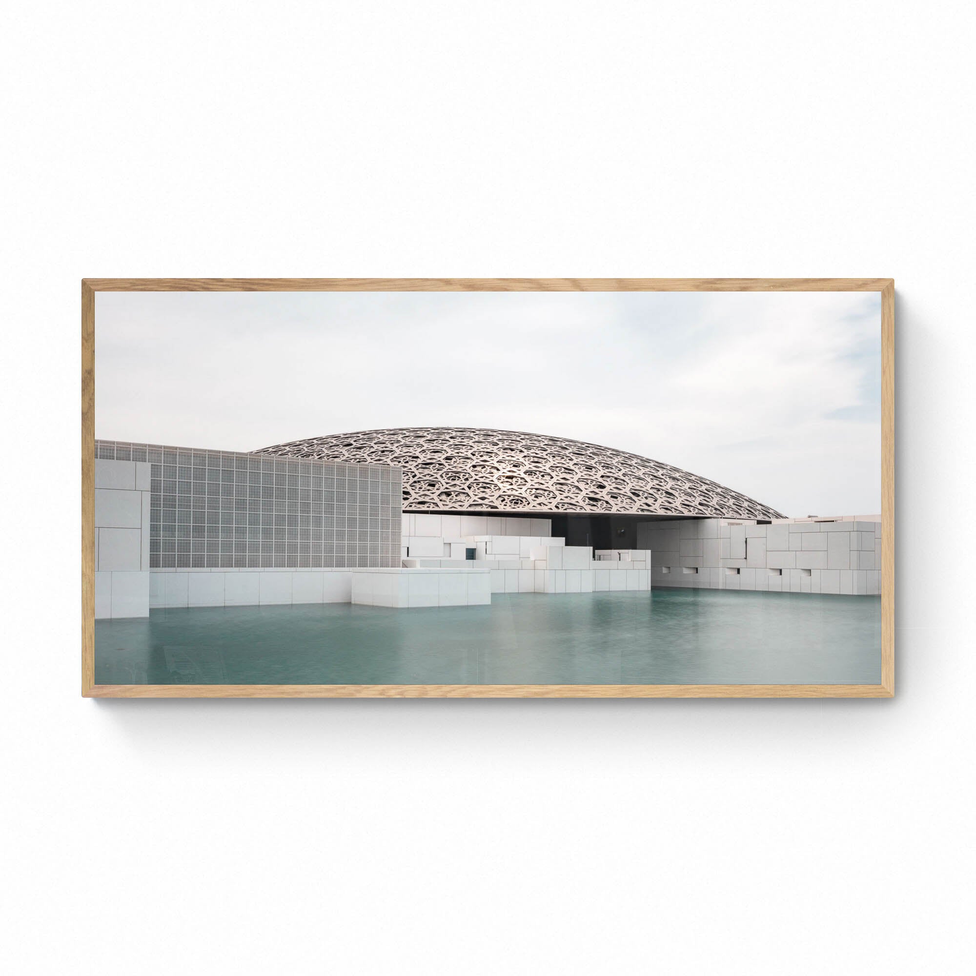 Wide-angle view of the Louvre Abu Dhabi’s intricate dome over calm water, under a soft sky.