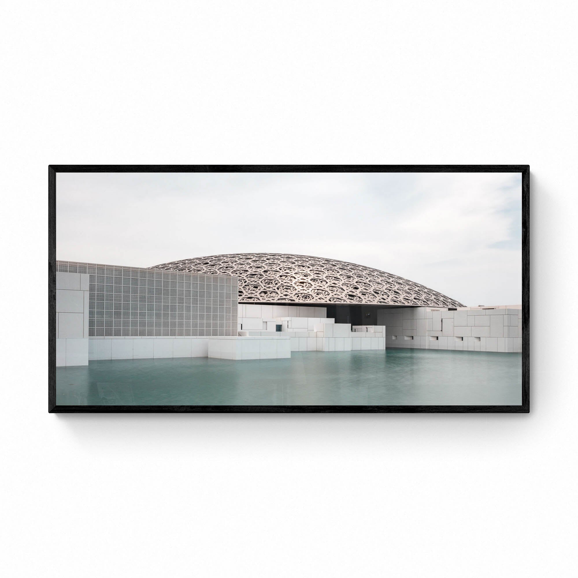 Wide-angle view of the Louvre Abu Dhabi’s intricate dome over calm water, under a soft sky.