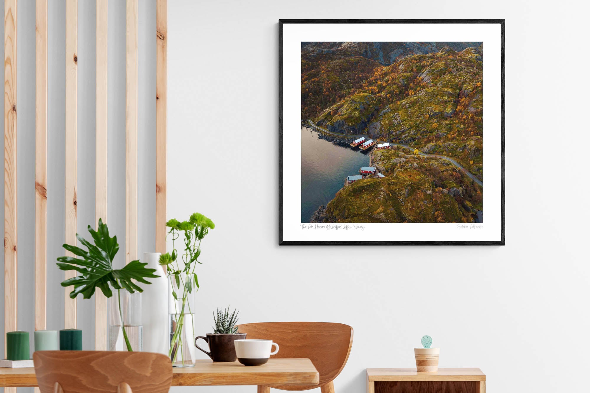 Aerial view of traditional red Norwegian cabins by the rocky shore of Nusfjord, Lofoten, amidst autumn-colored vegetation.