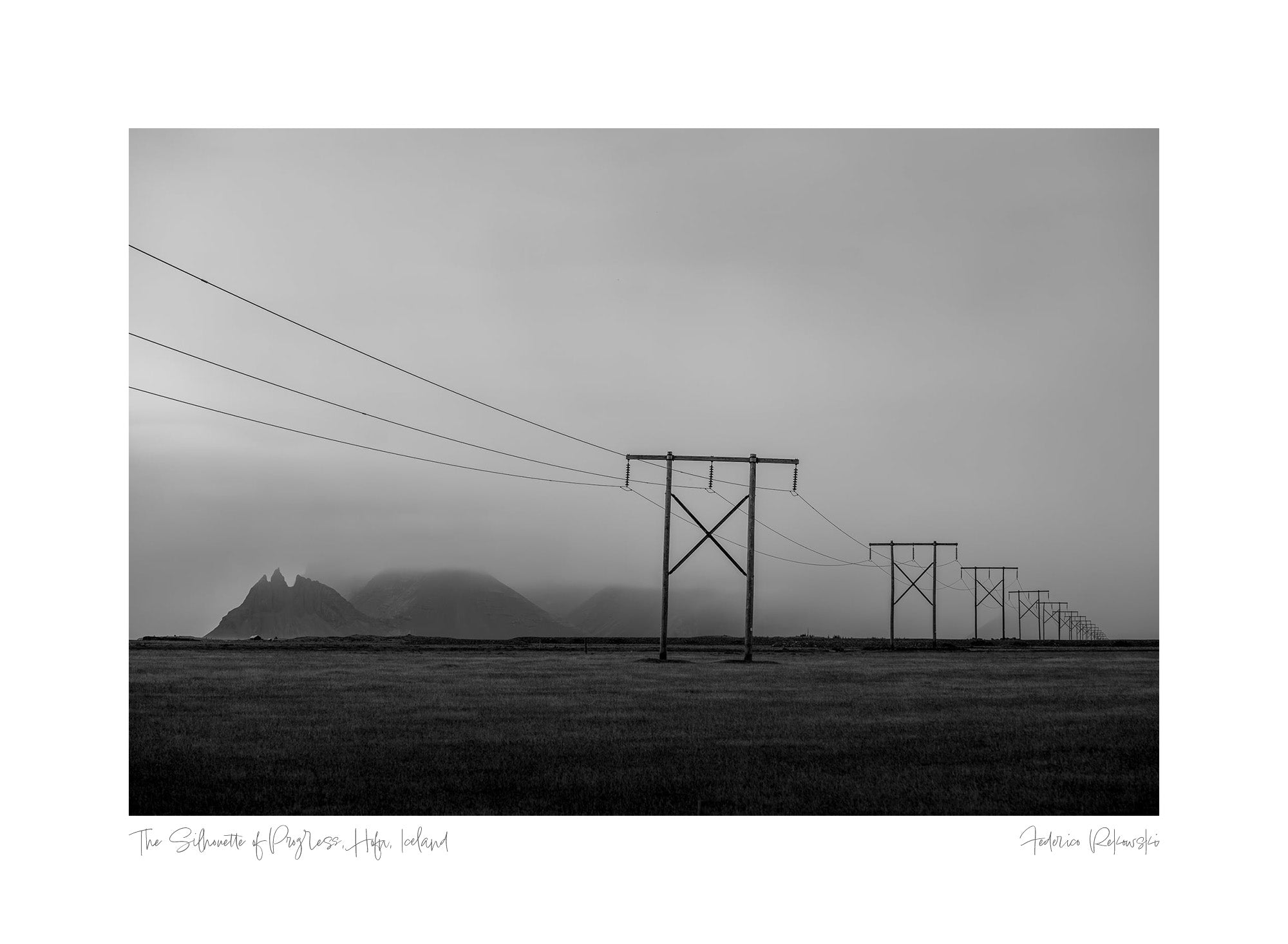 Black and white photo of power lines running across a field in Hofn, Iceland, with mountains faintly visible in the misty background.